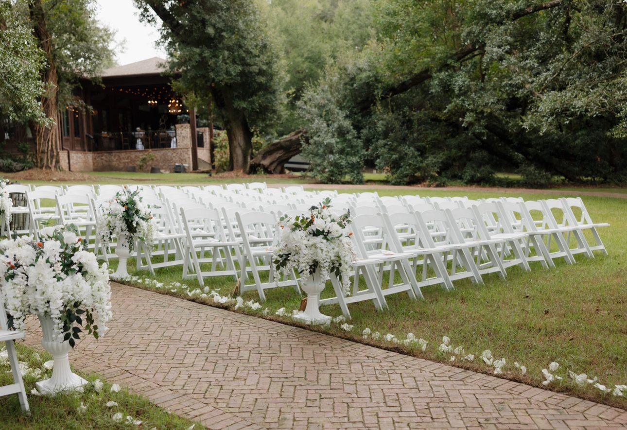 Outdoor wedding ceremony with white chairs.