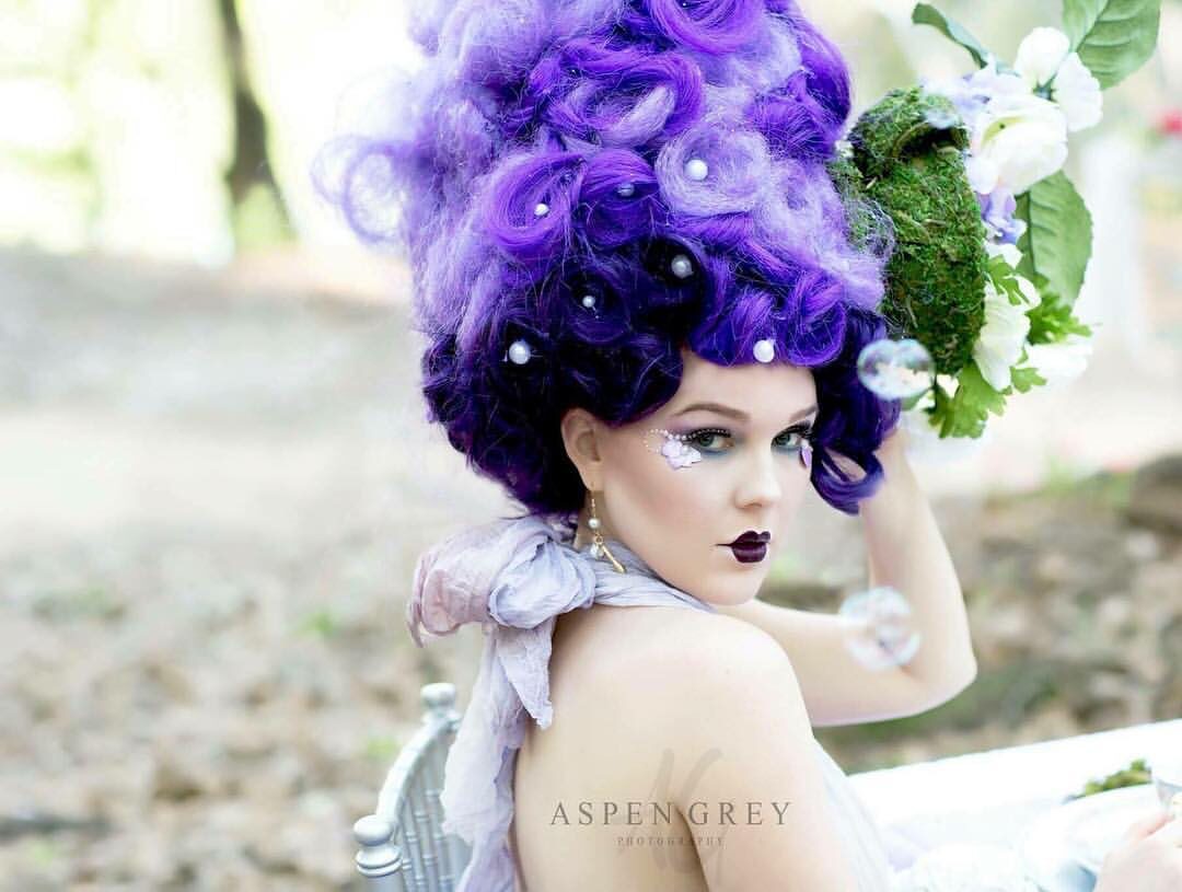 Woman in purple wig with flowers.