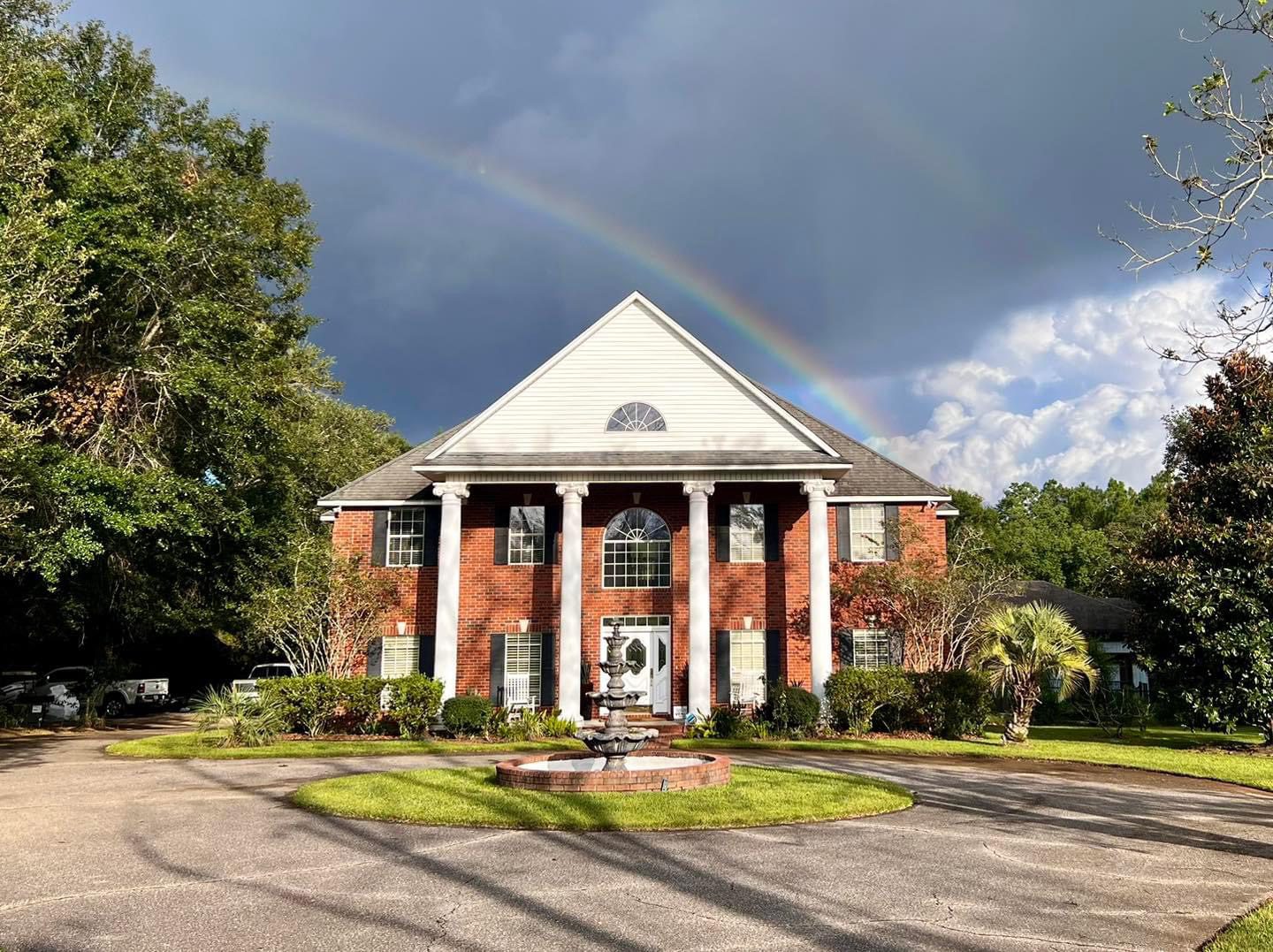 Brick mansion with rainbow, fountain.