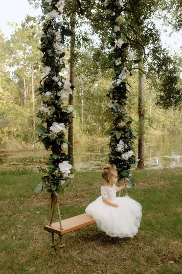 Girl in white dress on floral swing.