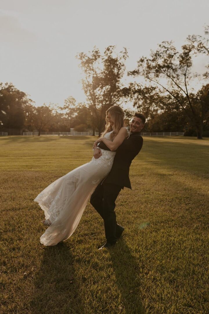 Groom happily lifts his bride outdoors.