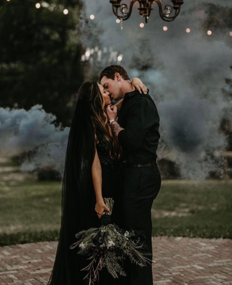 Couple in black, kissing amidst smoke.
