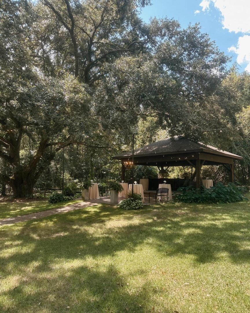 Outdoor wedding gazebo under large trees.
