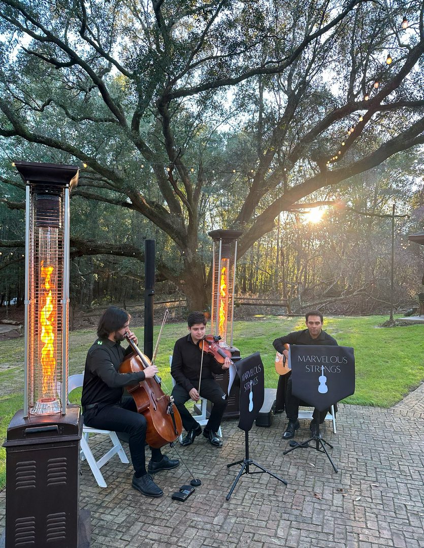 String trio performing outdoors by heaters.